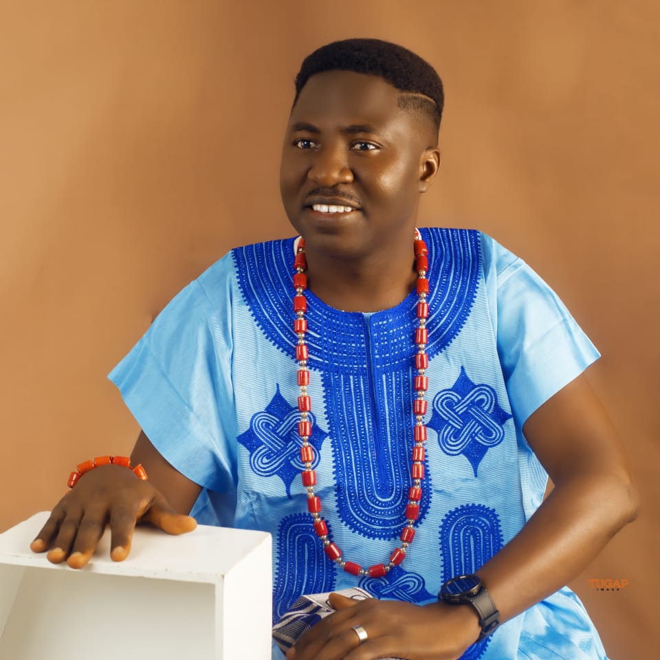 Man seated in a sky blue native outfit with bold royal blue embroidery and coral beads