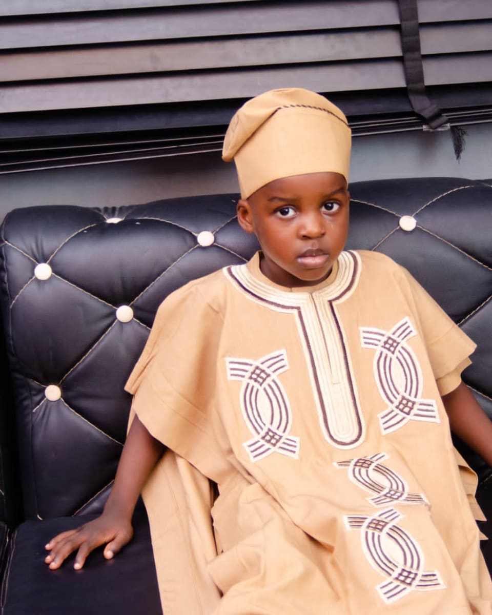 Young boy in a gold agbada and fila seated on a sofa