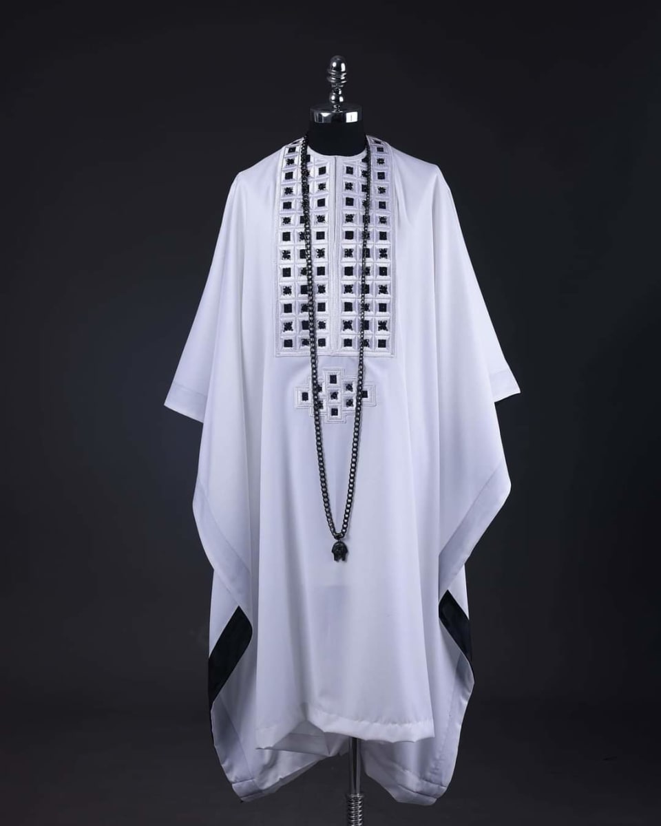 White agbada with black square embroidery and a long black bead necklace, on a mannequin