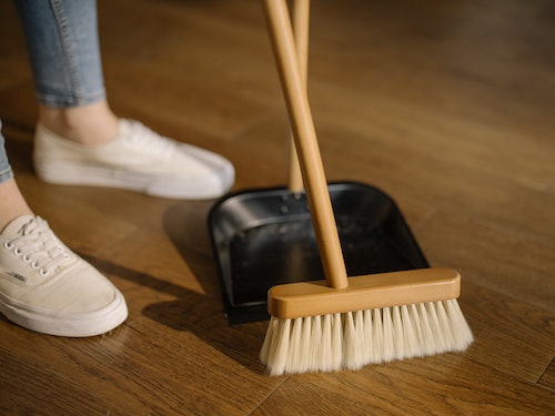 Person using broom to sweep into dust pan