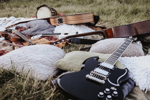 Guitars, fiddle, ukulel and bongo layed on pillows and blankets in a field.