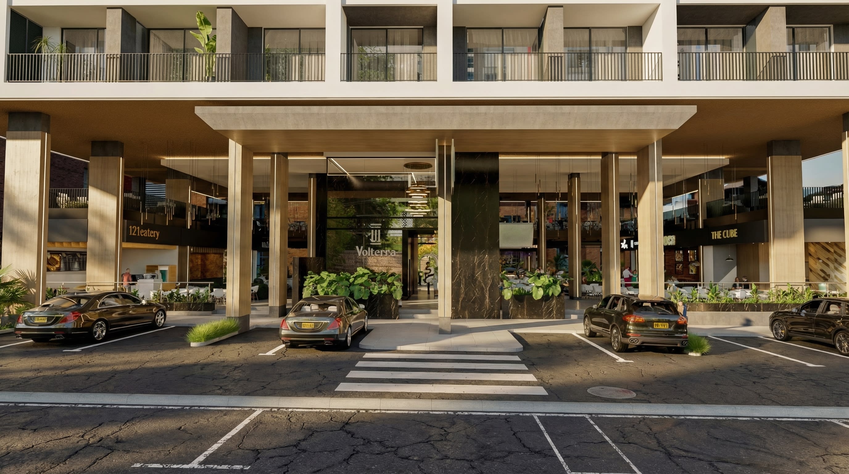 Fachada frontal de Volterra Plaza Suites con acceso vehicular y locales comerciales.