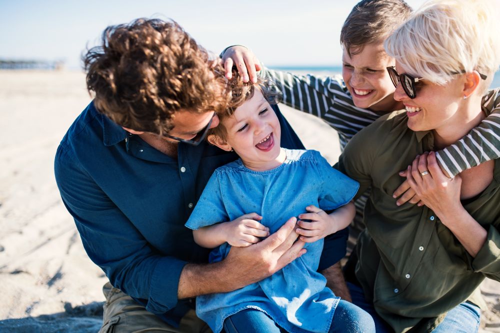 Young family with two small children sitting outdoors on beach, having fun