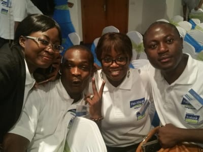 Des membres du personnel devant les panneaux de la nouvelle identité Pan-African Savings & Loans
