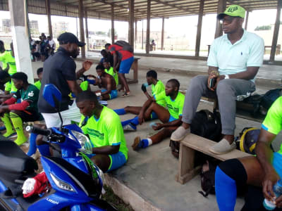 Des membres du personnel en maillot aux couleurs de PASL, assis sous un préau avant la rencontre