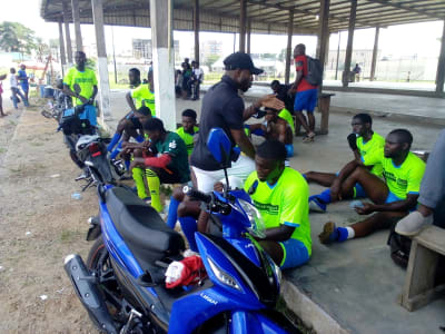 Des membres du personnel en maillot aux couleurs de PASL, assis sous un préau avant la rencontre