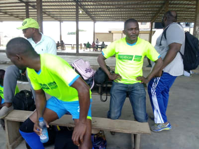 Des membres du personnel en maillot aux couleurs de PASL, assis sous un préau avant la rencontre
