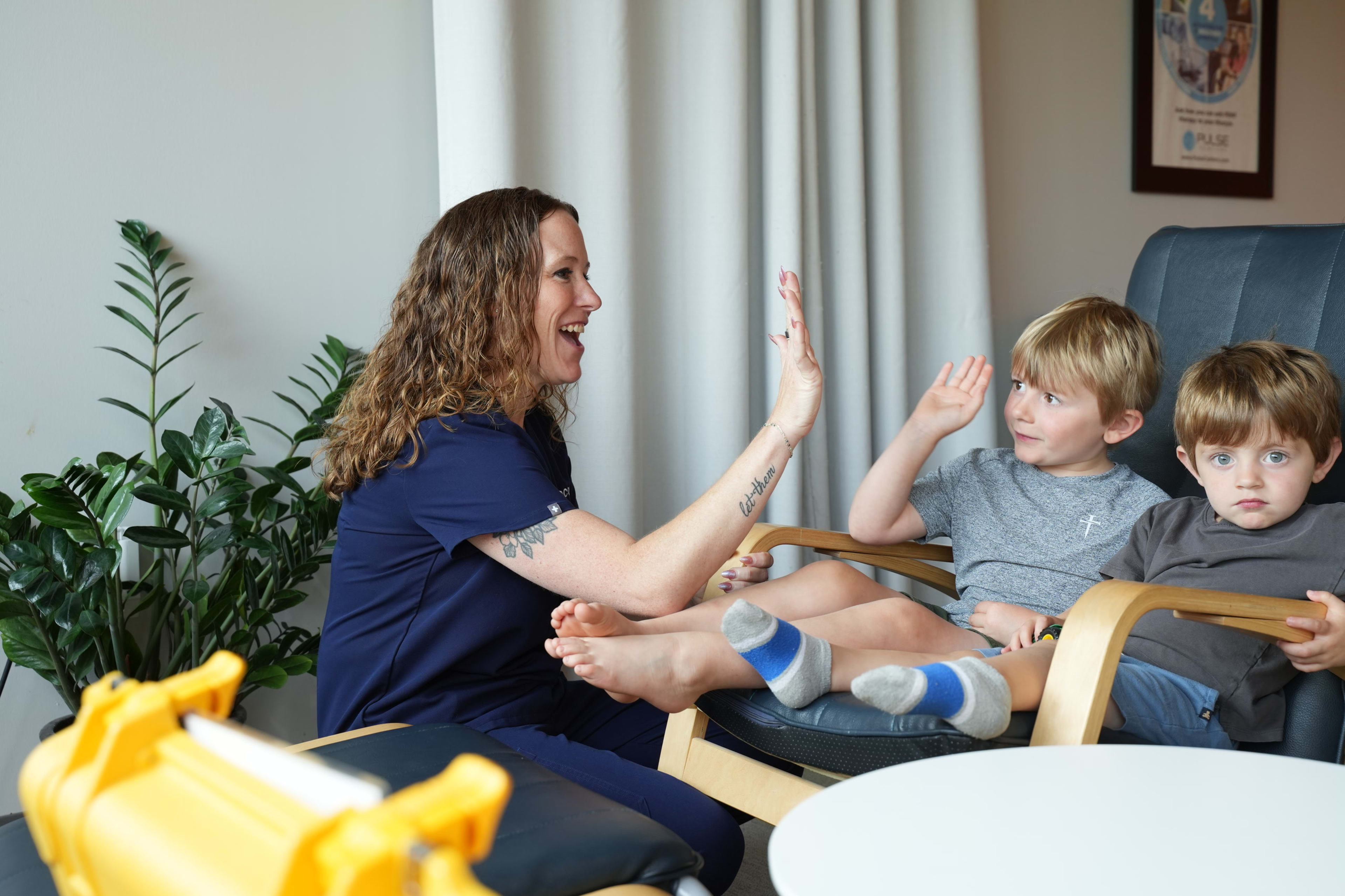 A clinician seated beside two young children in a treatment chair