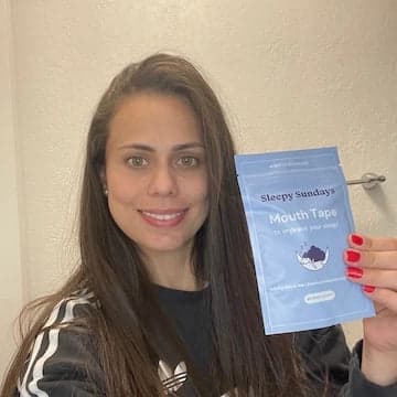 A woman holding a packet of 'Sleepy Sundays Mouth Tape' and smiling.