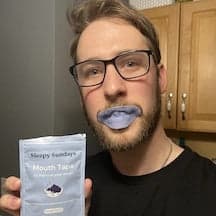 Man with glasses demonstrating a mouth tape product in a kitchen.