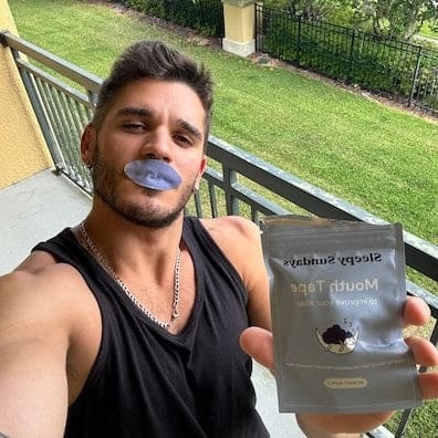 Man with tape covering mouth holding a 'Sleepy Sundays Mouth Tape' package on a balcony.