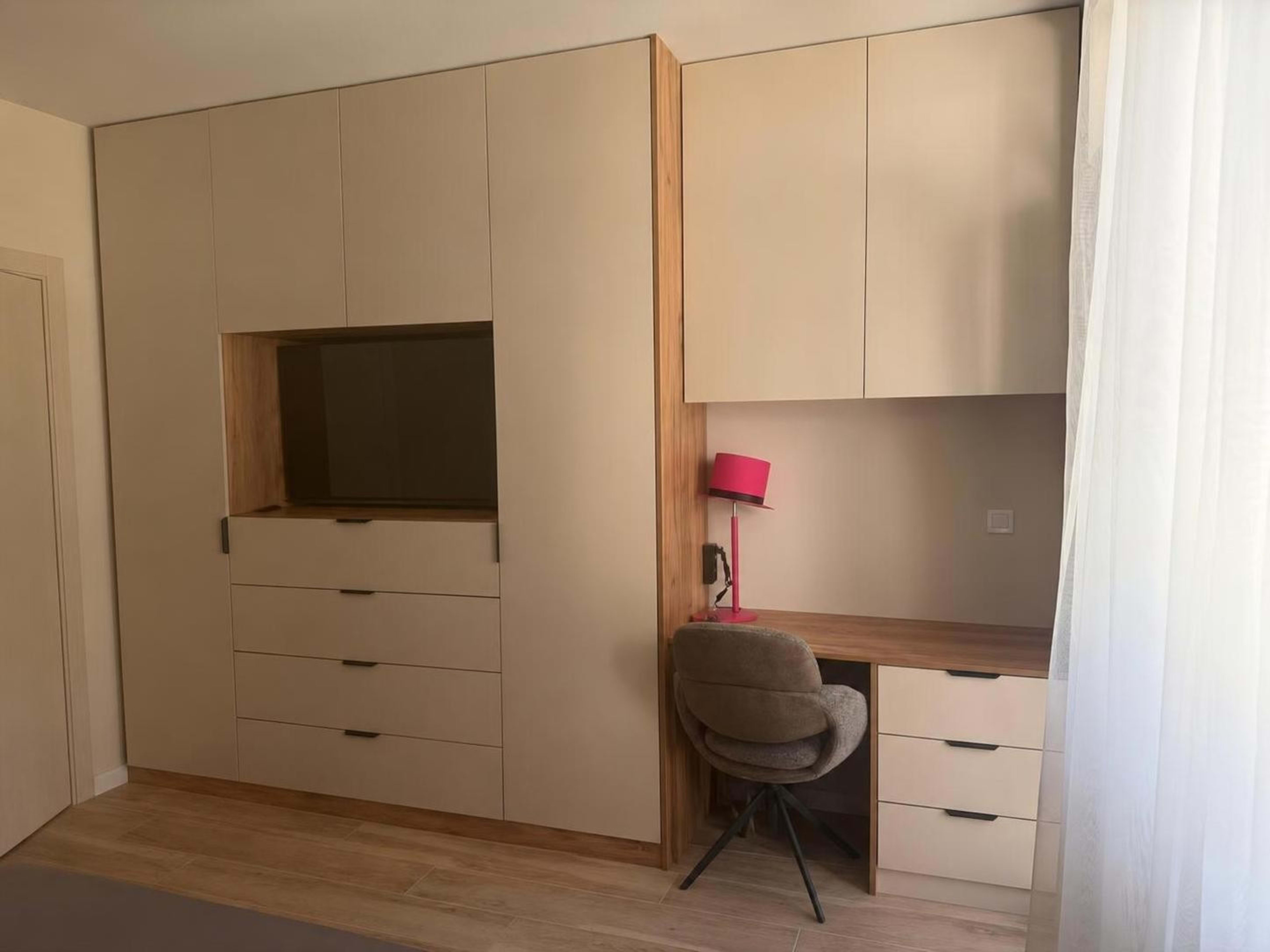 Bedroom with built-in light-coloured wardrobe cabinets, a TV niche, drawers, and a work desk.