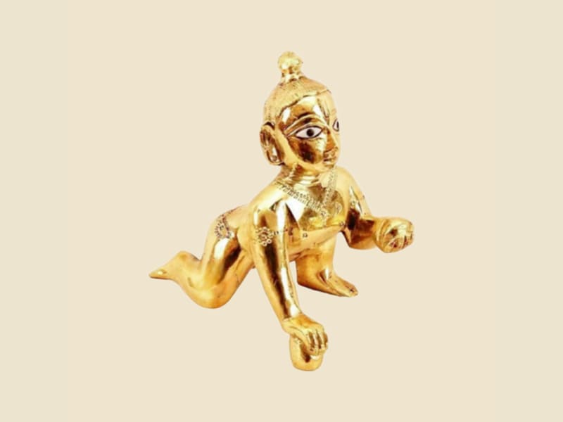 Polished Brass Laddu Gopal with Painted Eyes, Reaching Pose on a warm ivory background