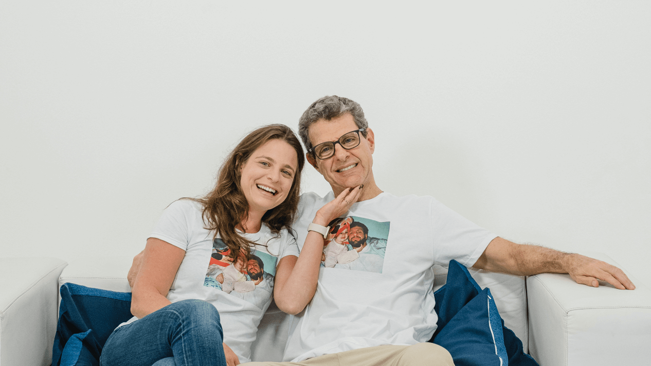 Mulher jovem sorrindo sentada ao lado do pai, que também está sorrindo