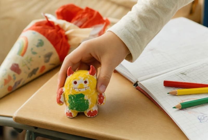 Kinderhand stellt eine selbst bemalte Monster-Figur auf den neuen Schulschreibtisch