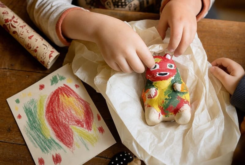 Kinderhände packen eine selbst bemalte Figur in Seidenpapier ein, daneben eine gemalte Karte