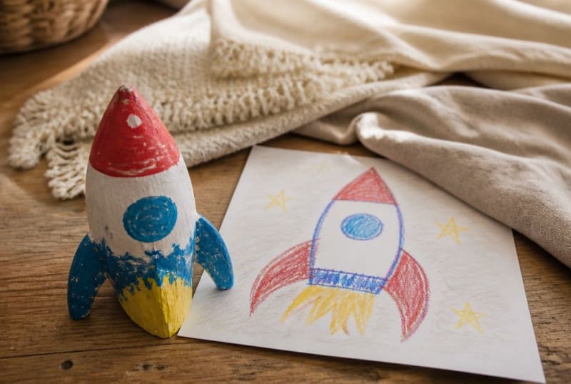 Kindgemalte Raketenfigur neben der Kinderzeichnung einer Rakete als Abschiedsgeschenk
