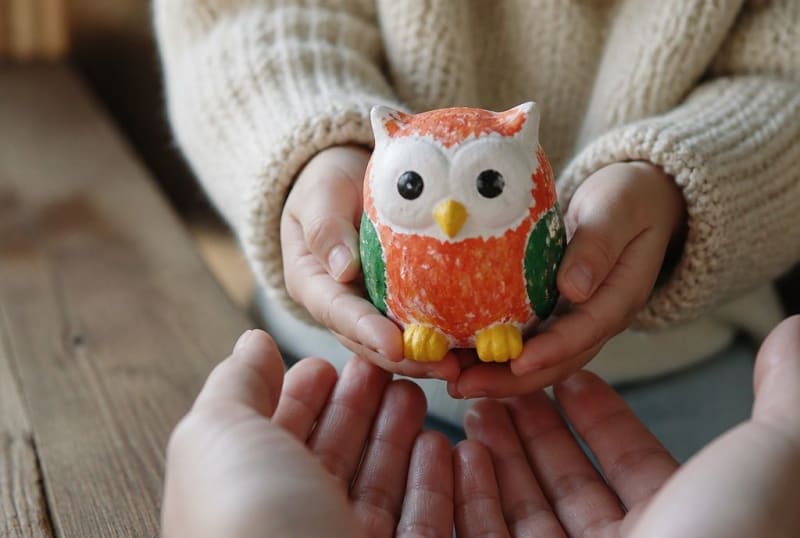Kinderhände zeigen einer Patin eine selbst bemalte Eulenfigur