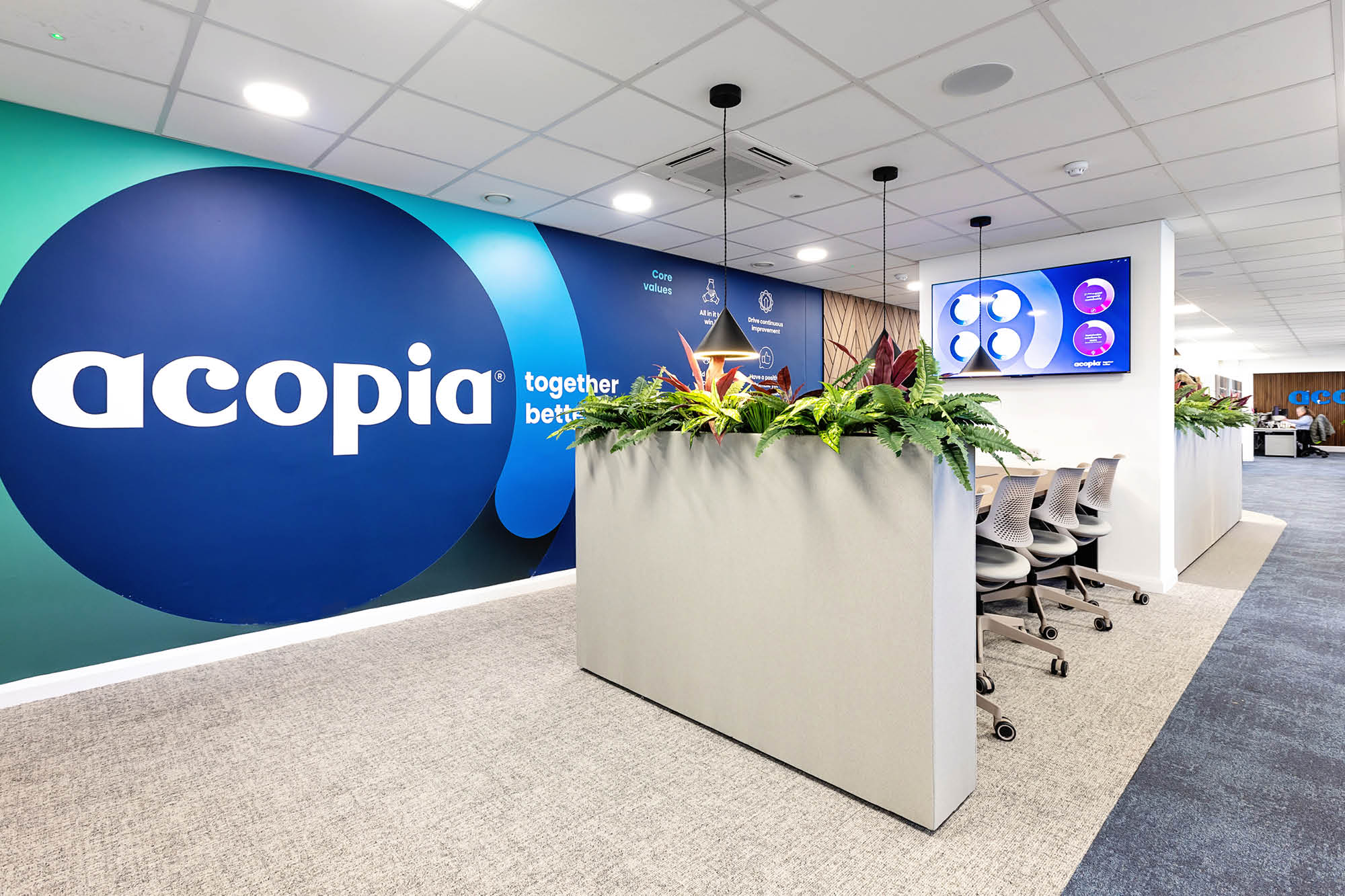 A modern office interior with a wall displaying the logo Acopia and the phrase together better. The space features a long planter.