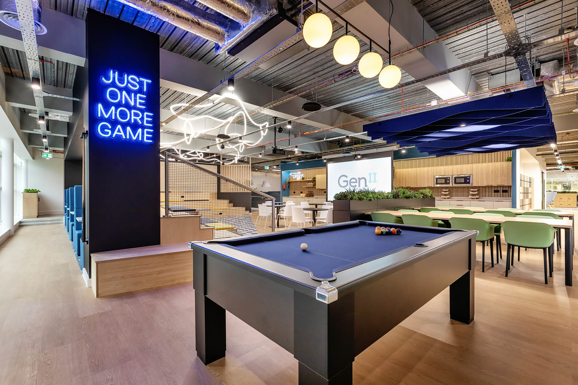 Modern office space with a black pool table in the foreground. Neon sign reads Just One More Game.