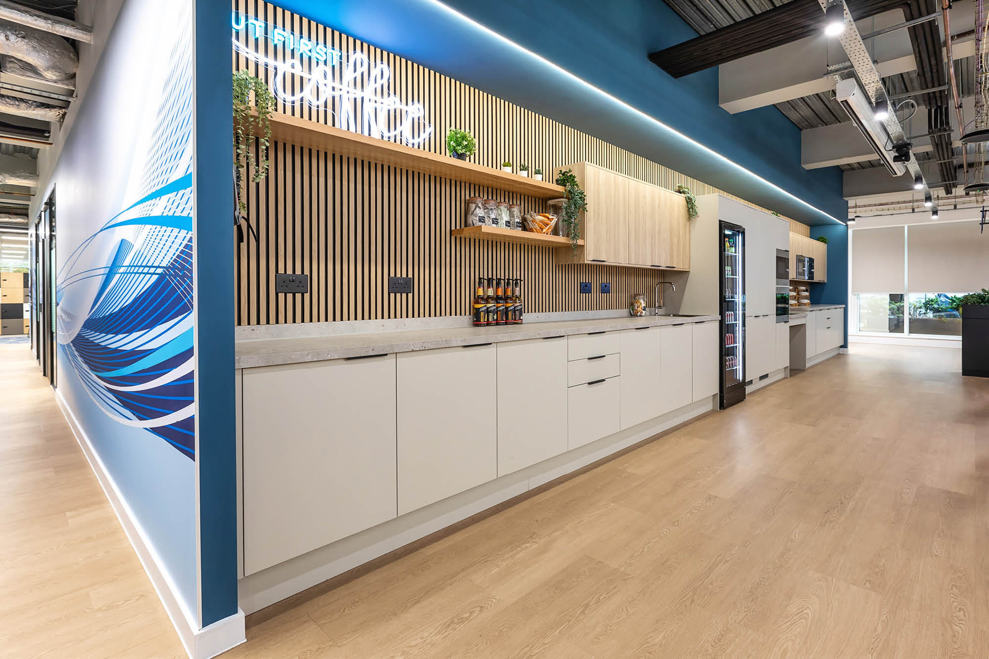 Modern office kitchen with sleek white cabinets, wooden accents, and a marble countertop.