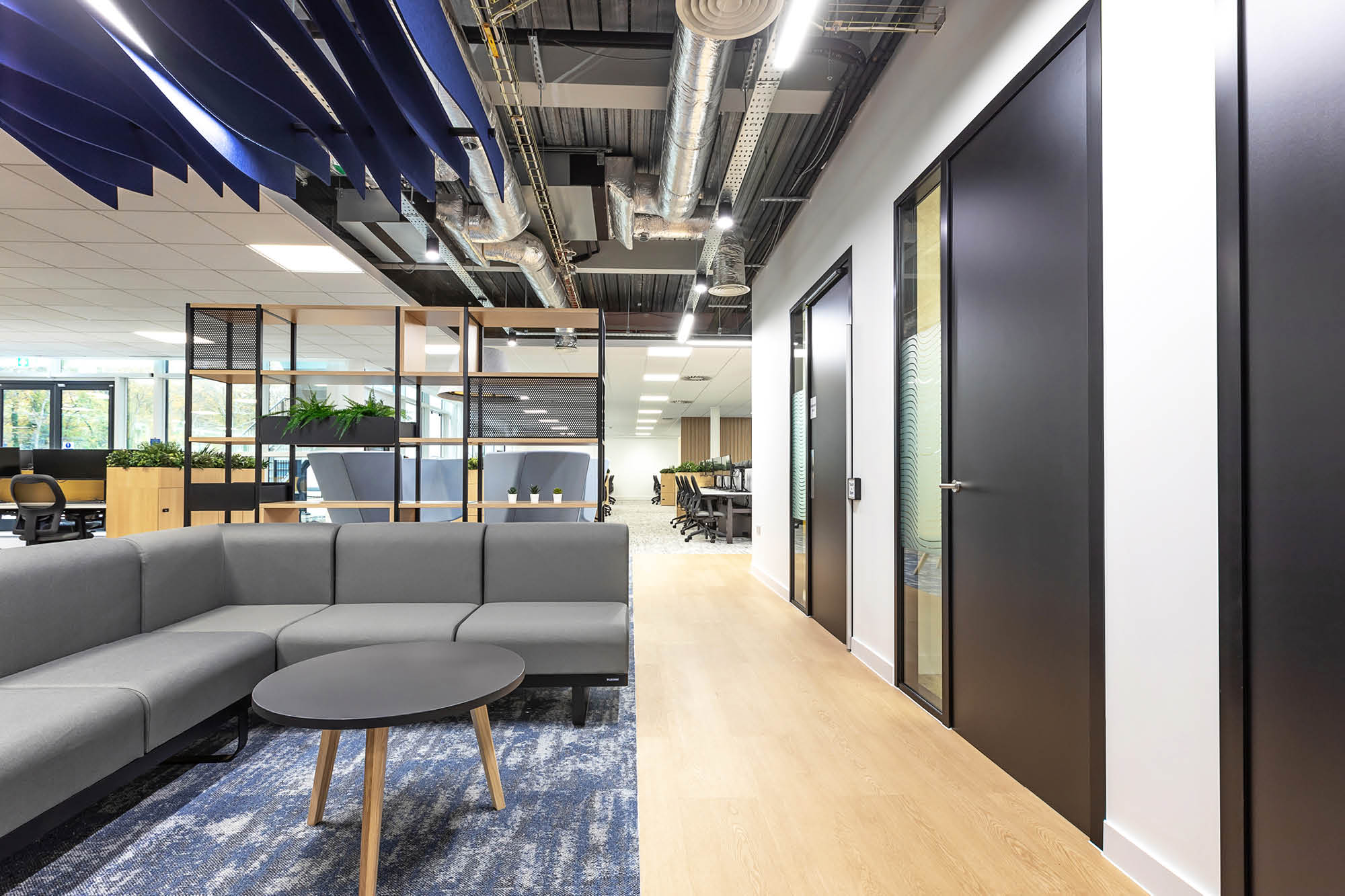 Modern office space with a grey sectional sofa and round table. Blue acoustic panels.