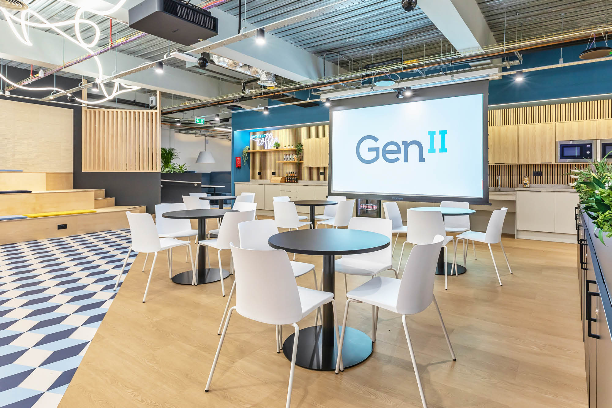 Modern meeting space with white chairs and round tables, a large screen displaying Gen II.
