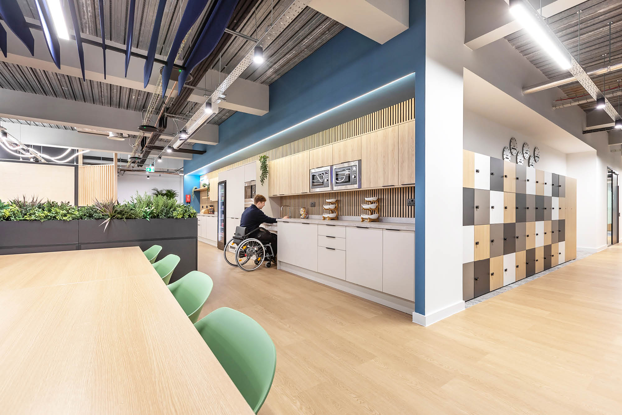 A modern office kitchen with a person in a wheelchair reaching for something on the counter.