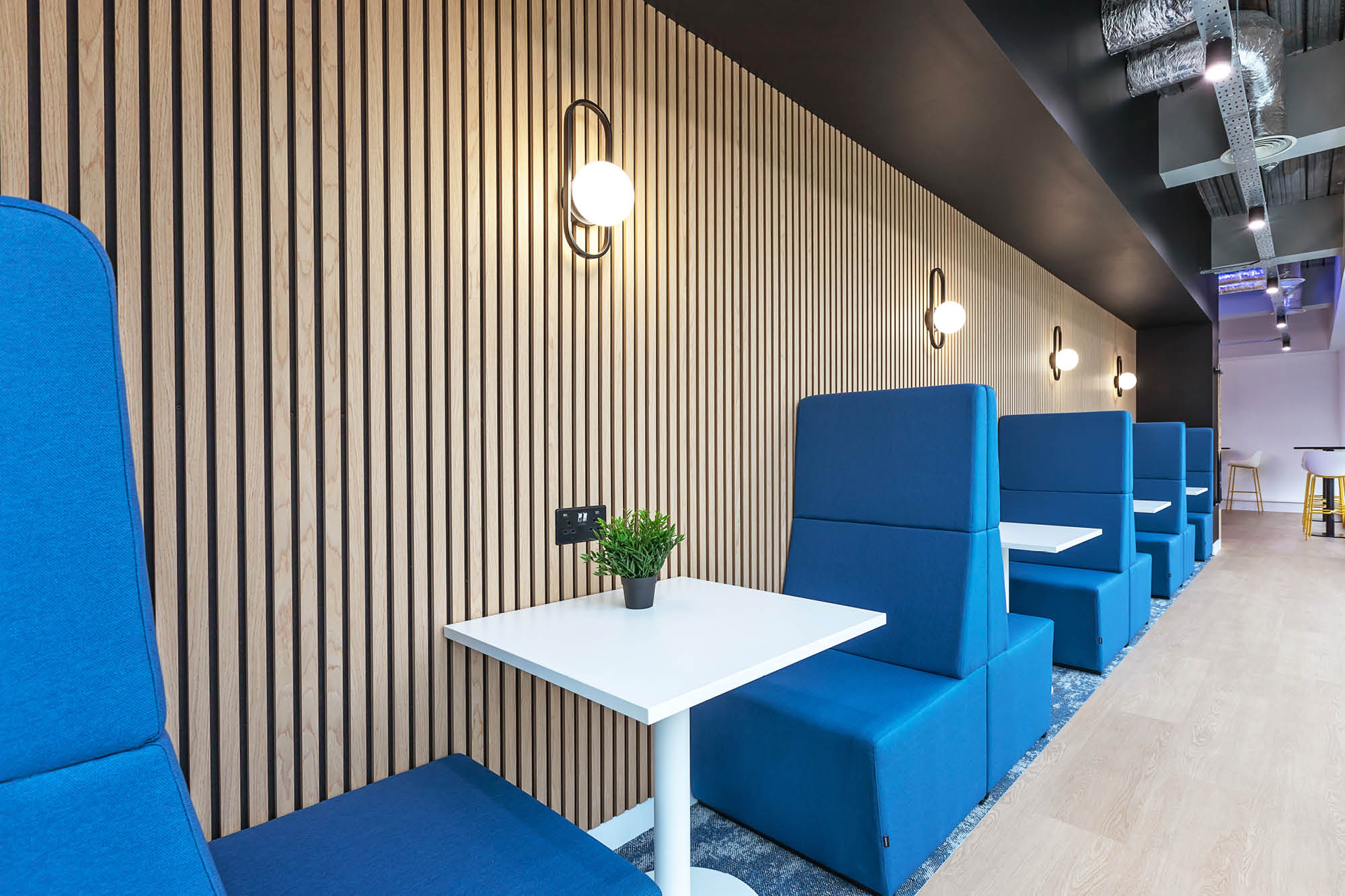 Modern seating area with blue high-backed booths and white tables against a wood-paneled wall.