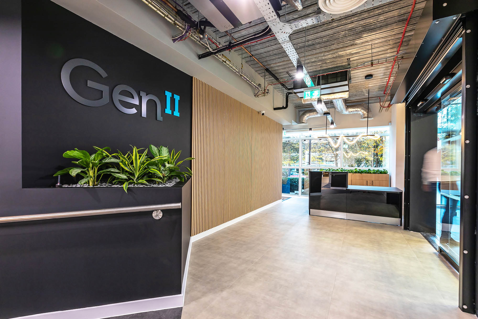 Modern office entrance with Gen II logo on a wall. There are plants in a small planter.
