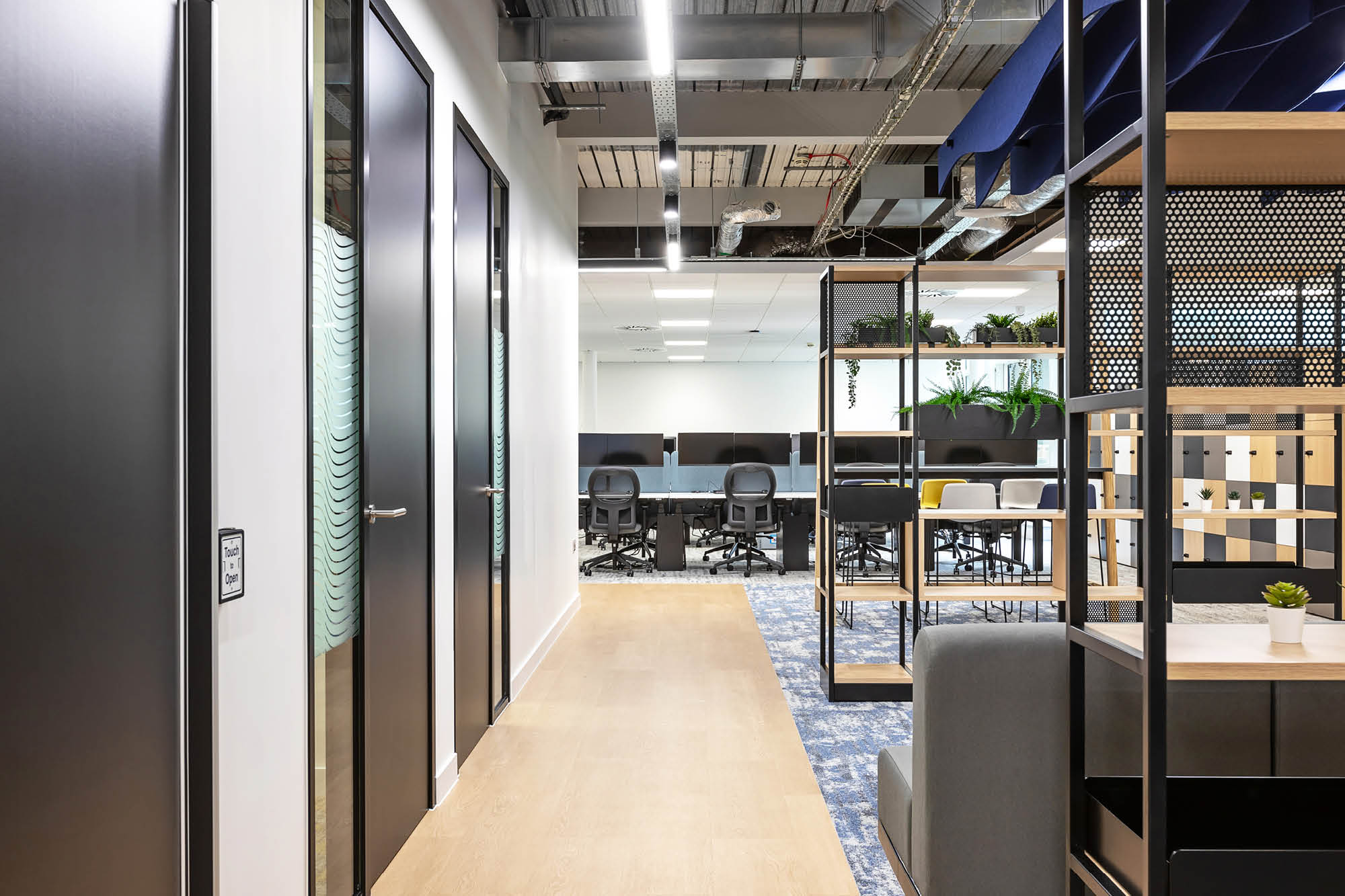 Modern office interior with a corridor leading to an open workspace. Features include black doors.