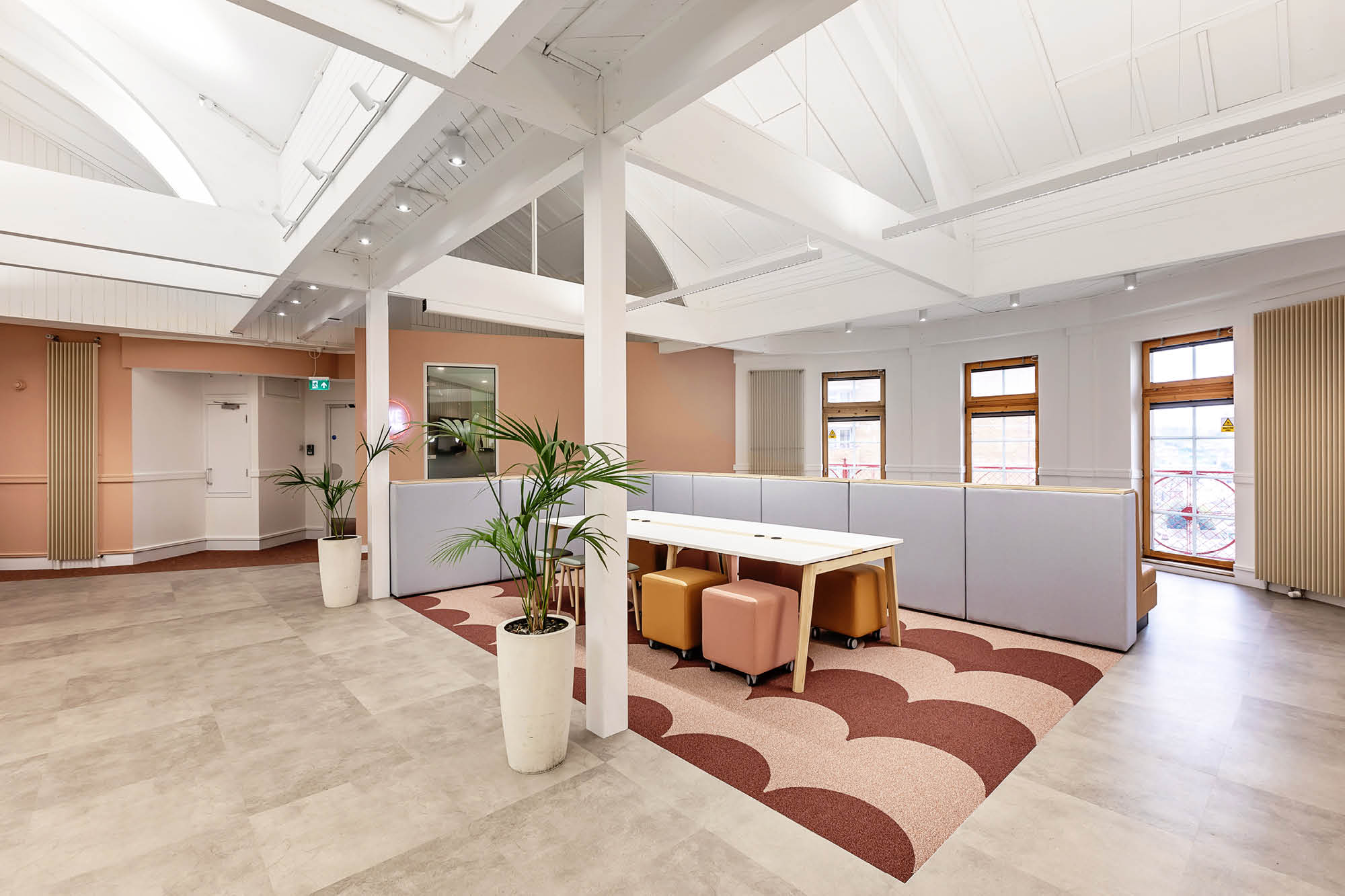 A modern office space with white walls and ceiling, featuring a central desk with four chairs.