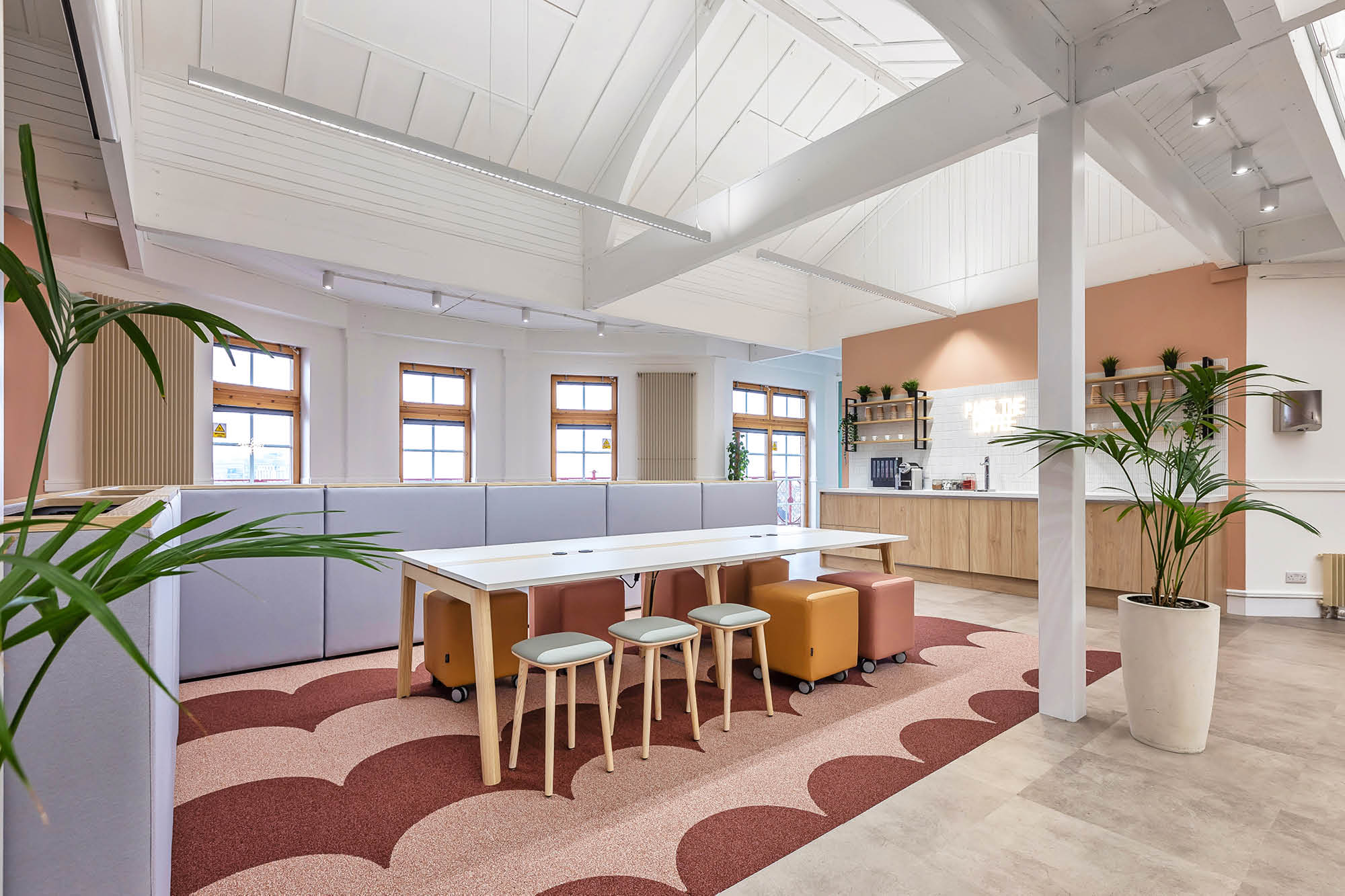 Modern open-plan office space with high ceilings, white walls, and wooden beams.