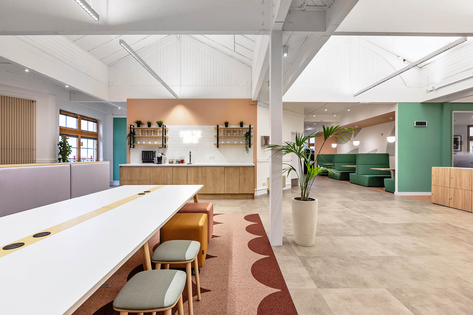 Modern office with long white table, colourful stools, and a patterned rug in the foreground.