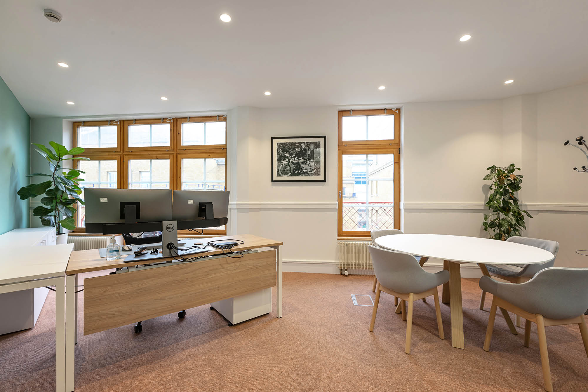 A bright office space with a wooden desk, dual monitors, and an office chair on the left.