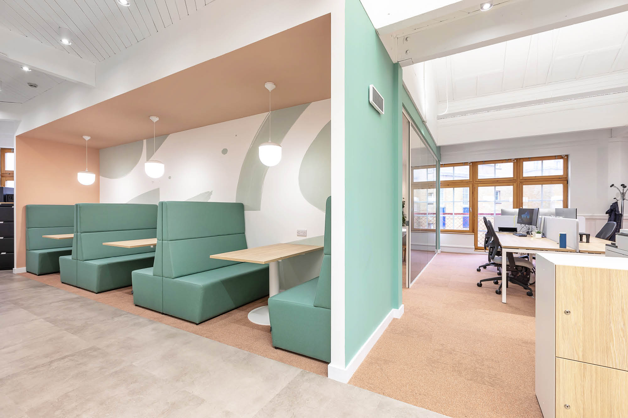 Modern office space with mint green booth seating and pendant lights on the left.