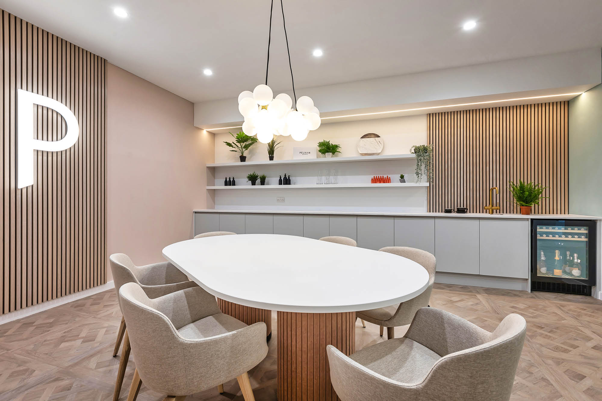 A modern meeting room with a white oval table, surrounded by six beige chairs.
