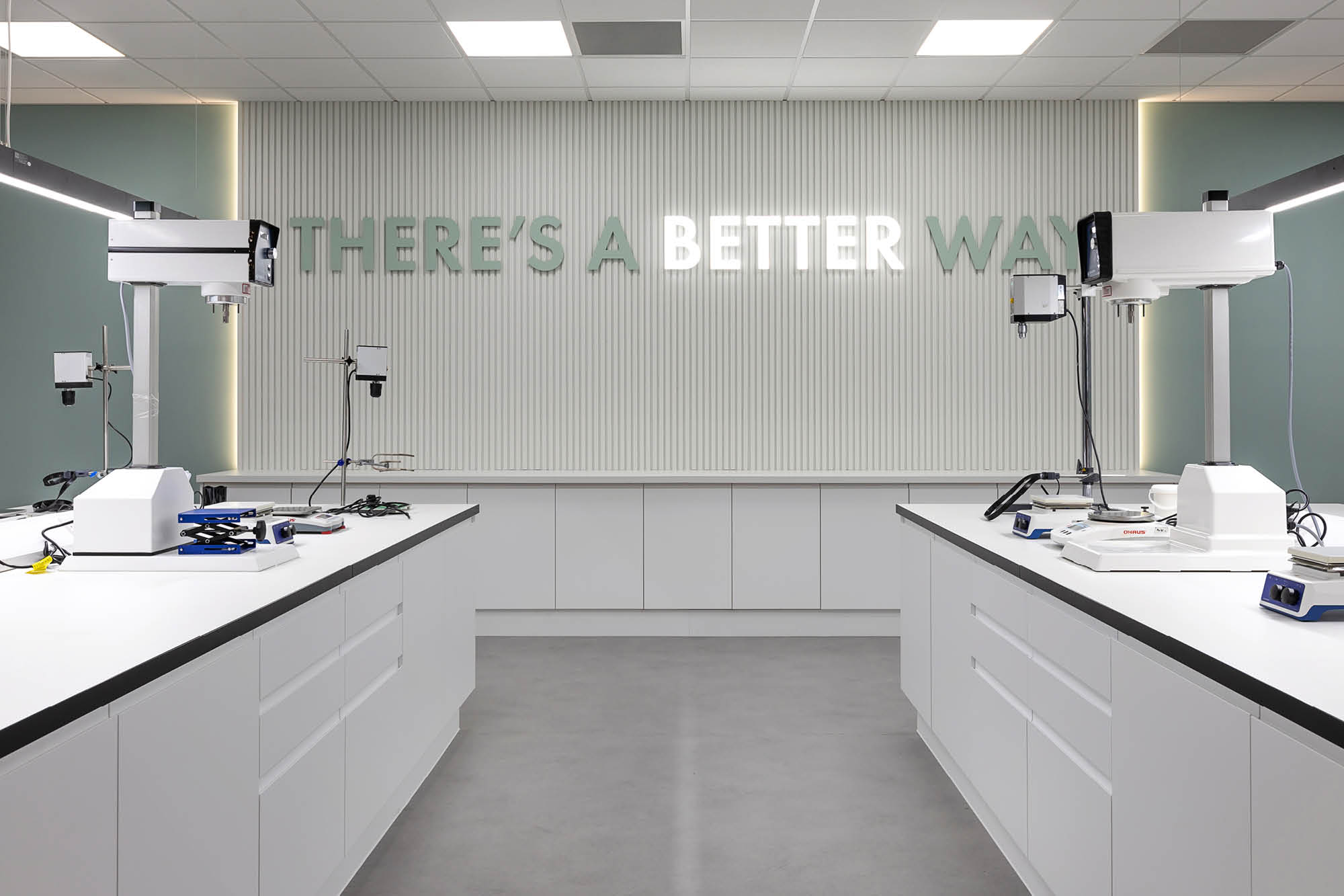 A modern laboratory with white workstations and equipment. The back wall features illuminated text.
