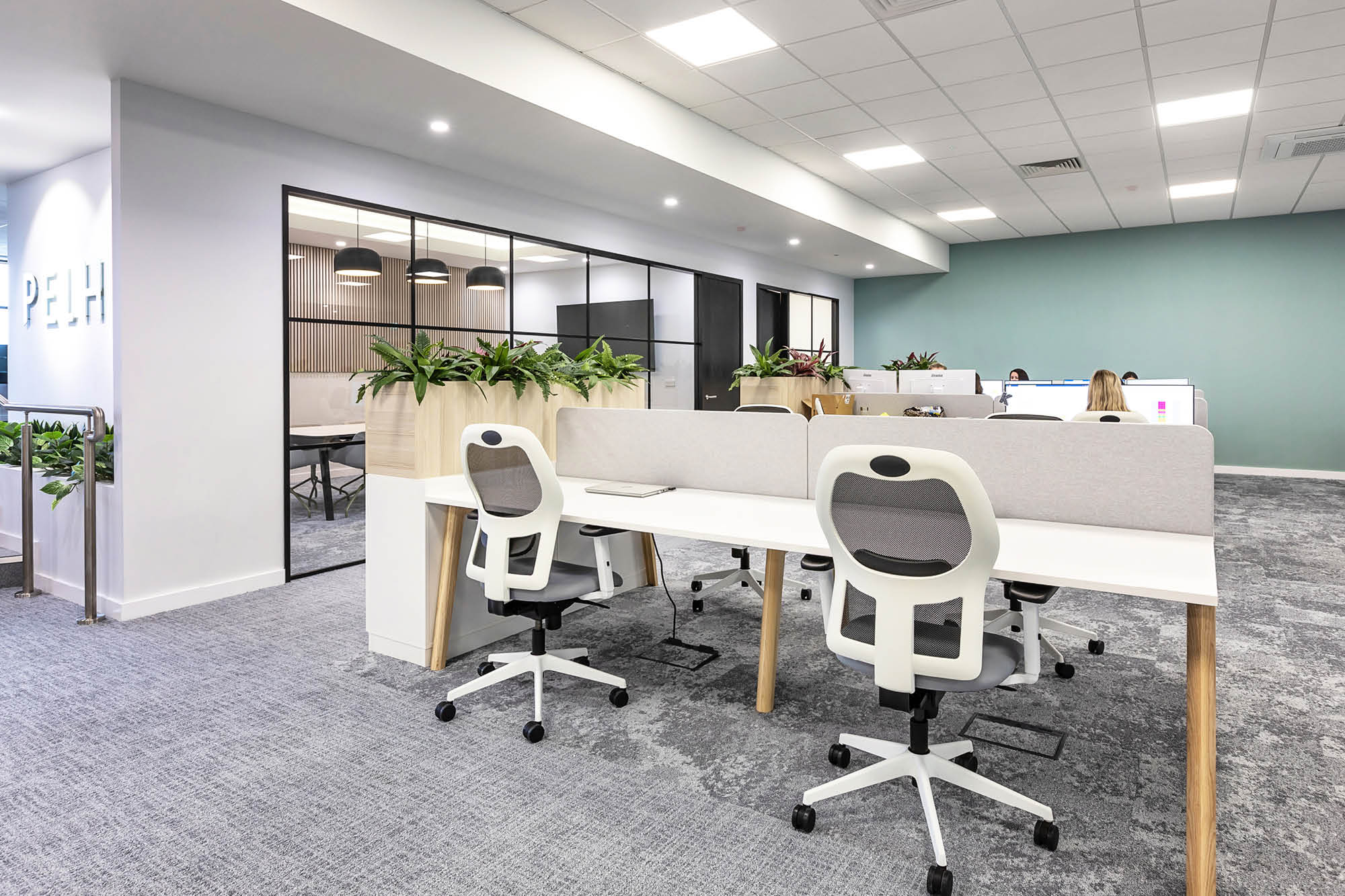 Modern office space with white desks and ergonomic chairs. Dividers separate workstations.