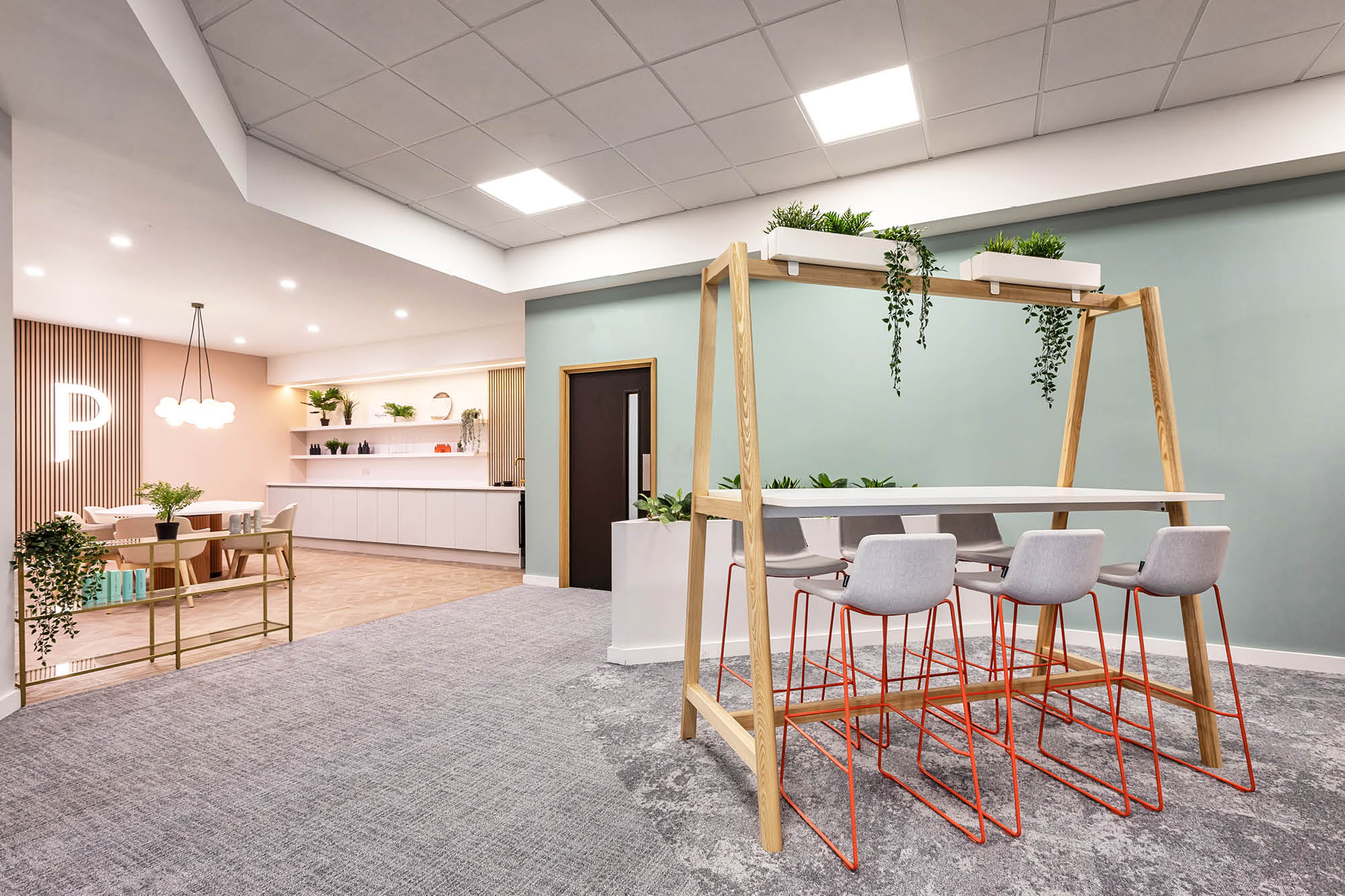 Modern office space with a high table and bar stools, featuring hanging plants.