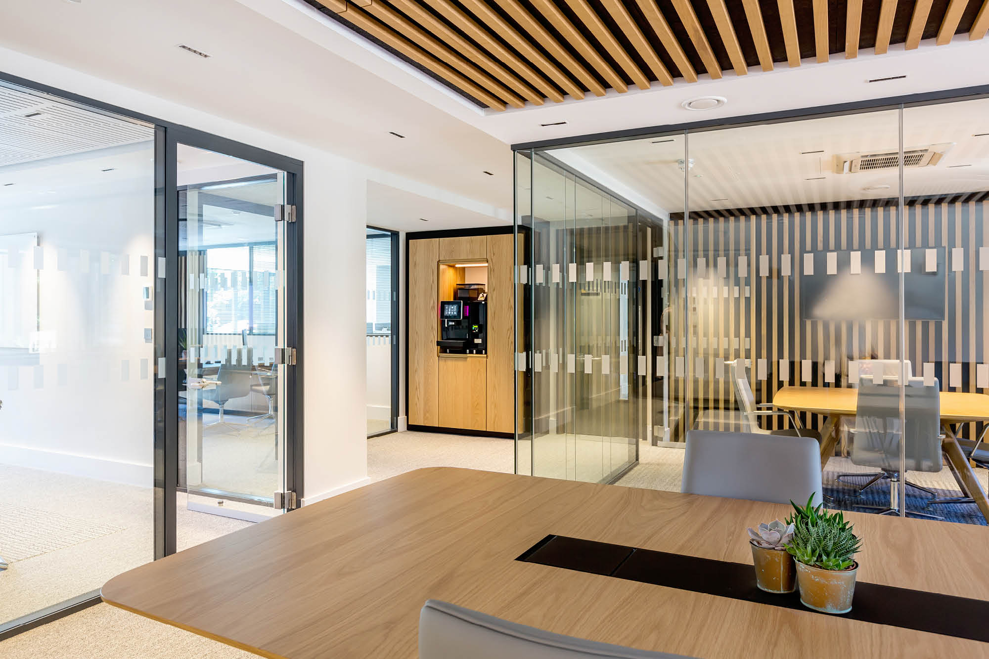 Modern office space featuring glass walls, a wooden table with a succulent plant, and a coffee machine in the corner.