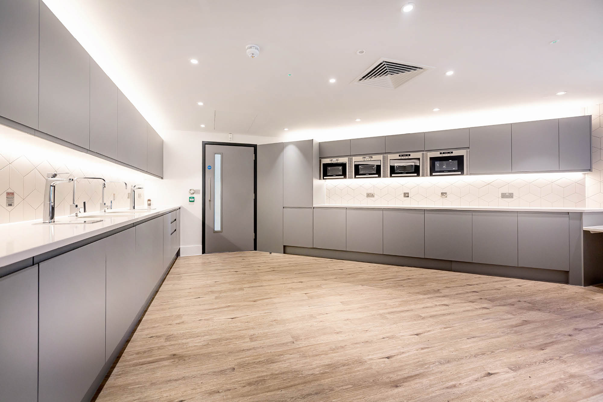 Modern kitchen with light wood flooring, gray cabinets, and integrated appliances. Overhead lighting brightens the space.