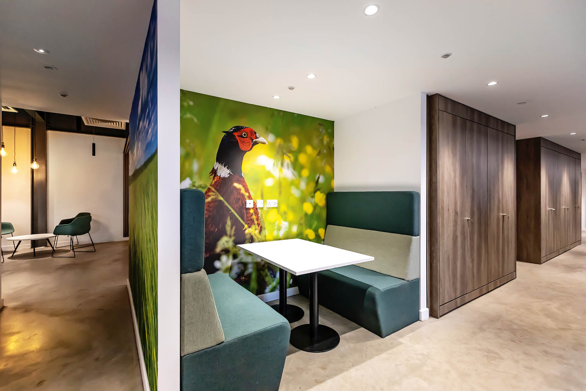 Modern seating area with a booth featuring green cushioned seats and a white table, set against a wall mural.