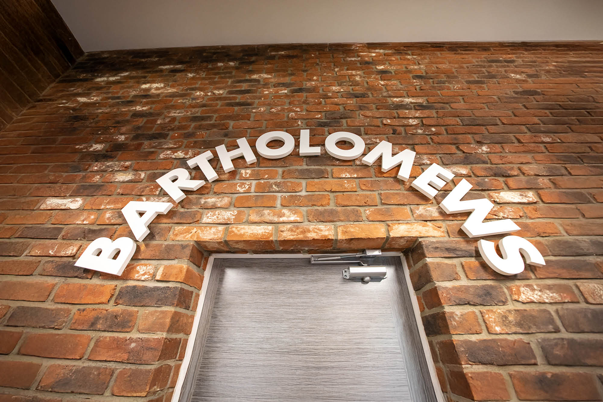 Bartholomews in white letters is arched above a door on a brick wall.