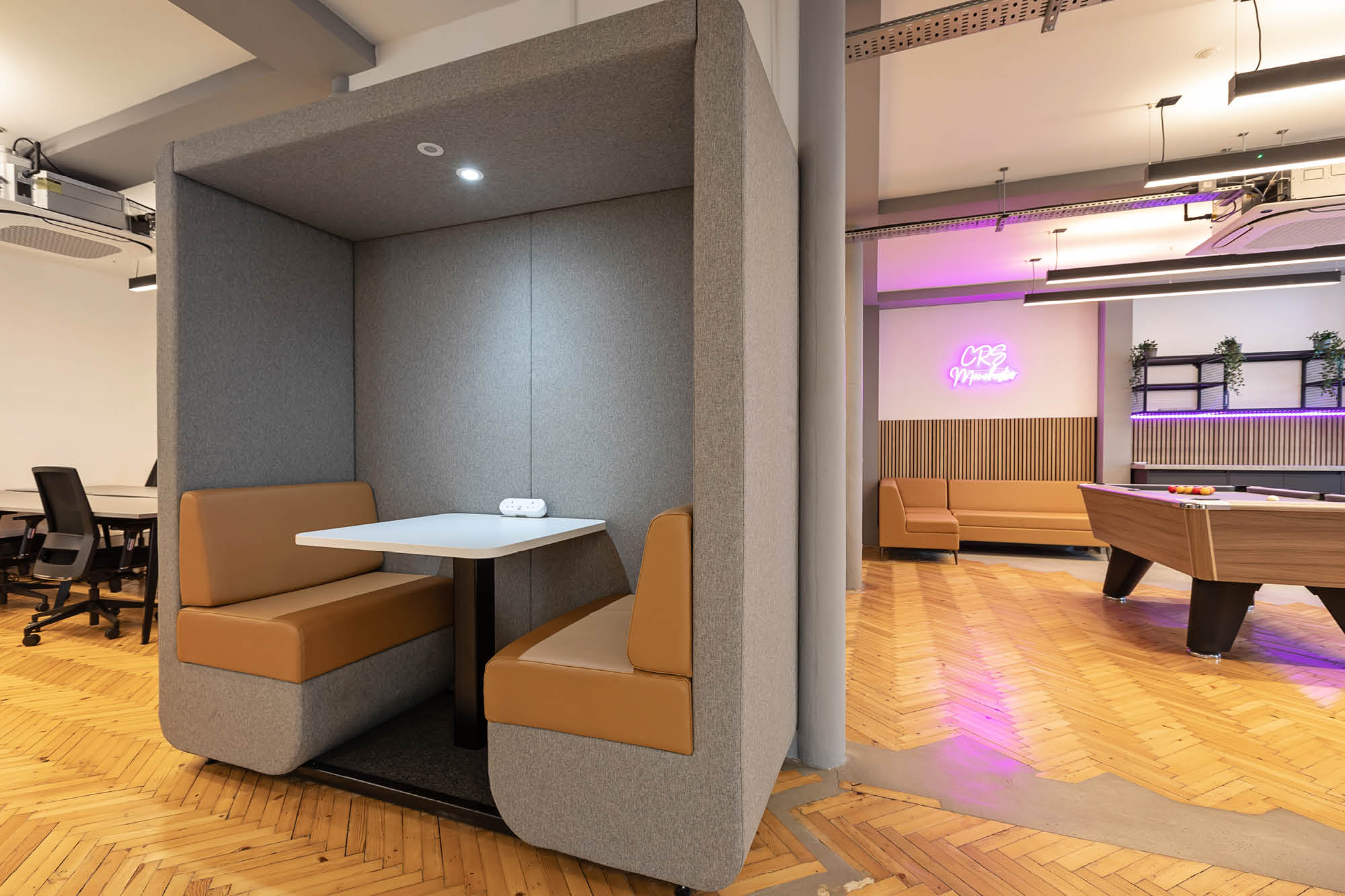 Modern office space with a cozy booth featuring brown cushioned seats and a white table. The open floor includes a pool table.