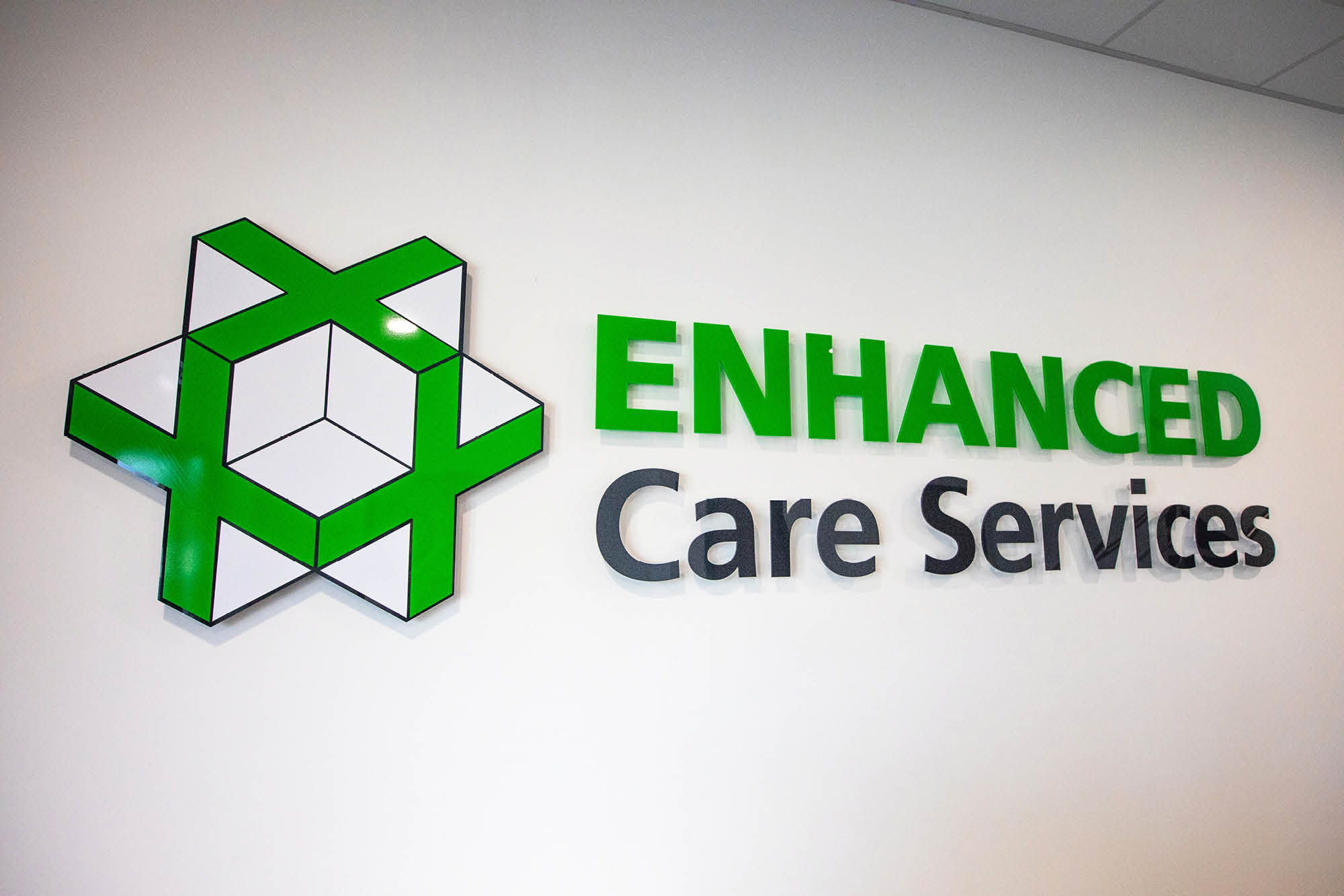 Logo on a wall with a geometric design featuring green and white interconnected blocks, next to the text ENHANCED Care Services in green.