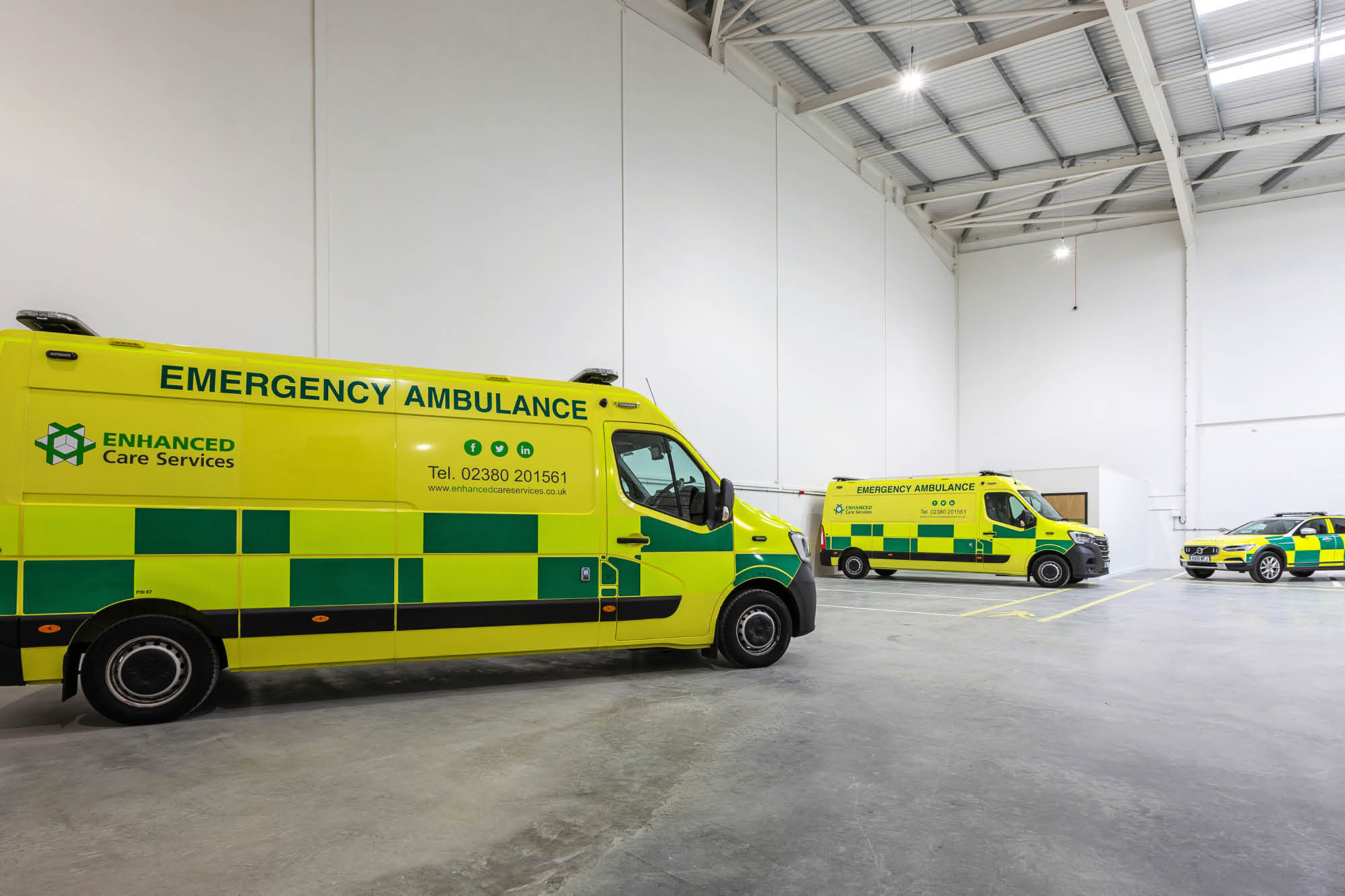 Three bright yellow emergency ambulances with green stripes are parked inside a spacious, well-lit garage.