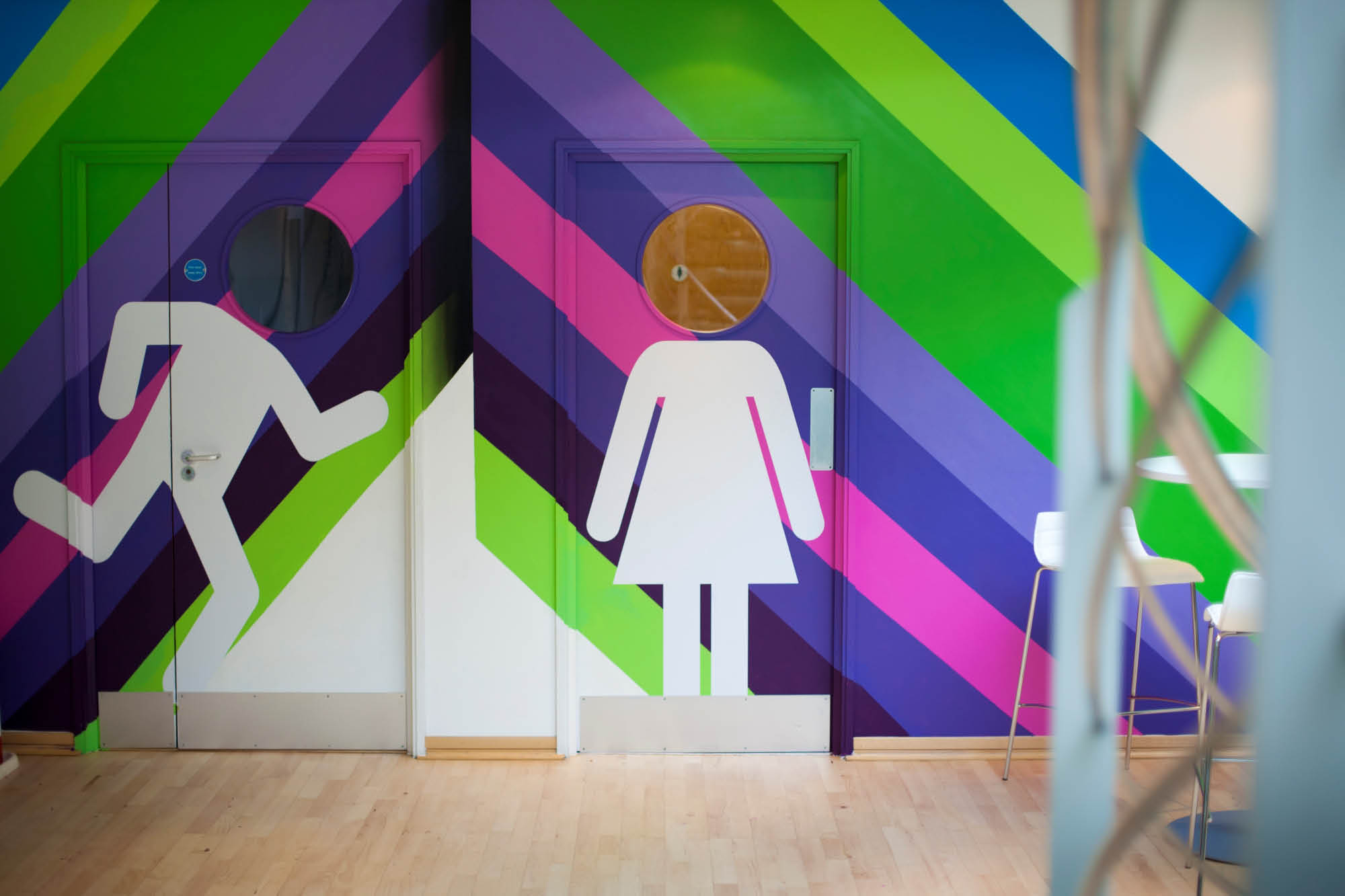 Colorful restroom doors with geometric patterns. The left door shows a figure running, while the right door displays a figure with a skirt.