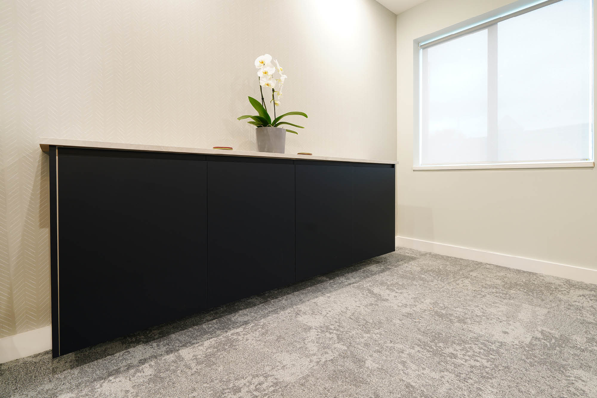 A minimalist room with a sleek black cabinet against a cream wall. A potted orchid with white flowers sits on top of the cabinet.