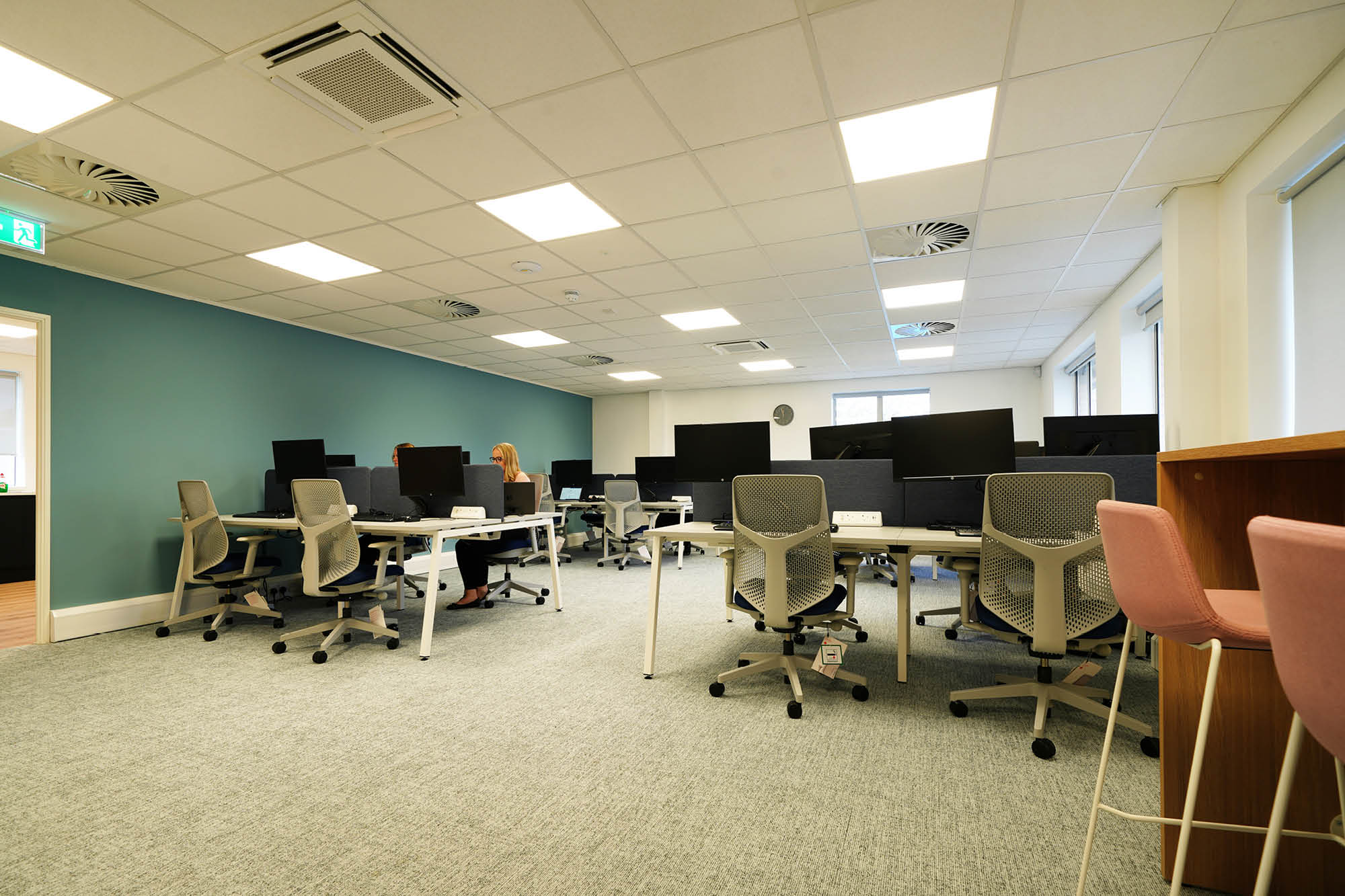 Modern office space with rows of empty desks, each equipped with computers and ergonomic chairs.